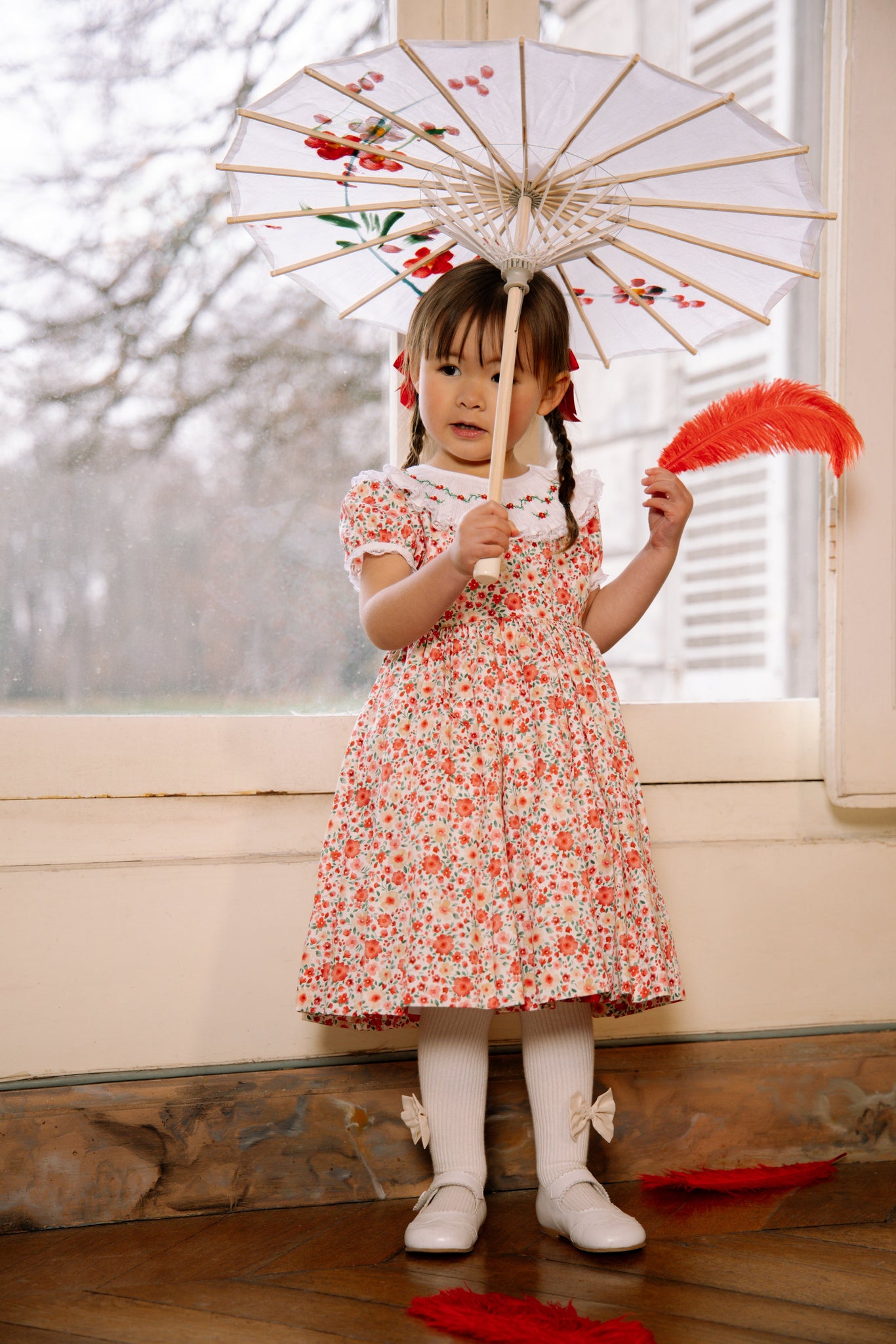 Young girl in Celestine Red Floral Smocked Dress holding a decorative umbrella indoors.