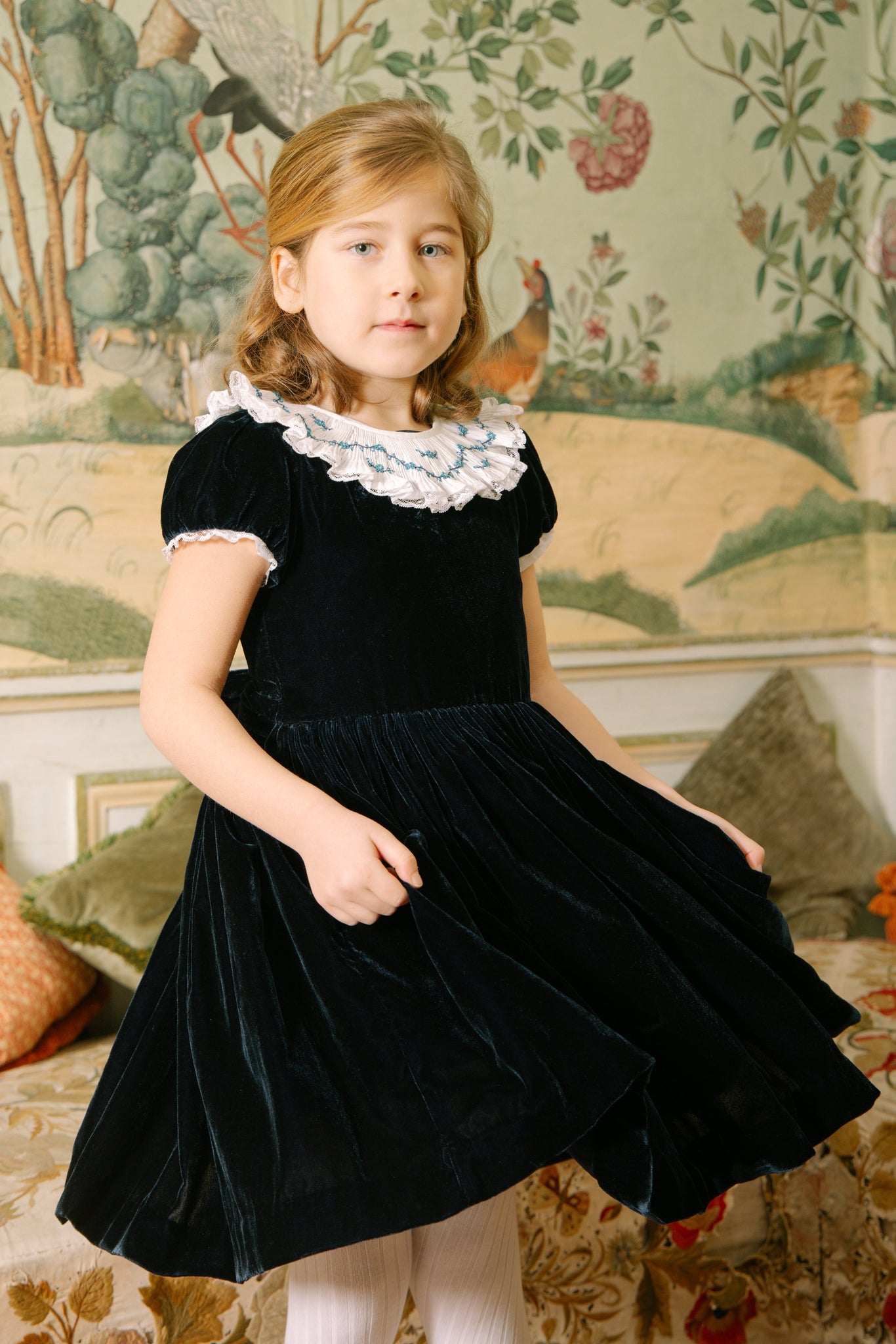 Young girl in Celestine Navy Velvet Smocked Dress standing in a decorated room.