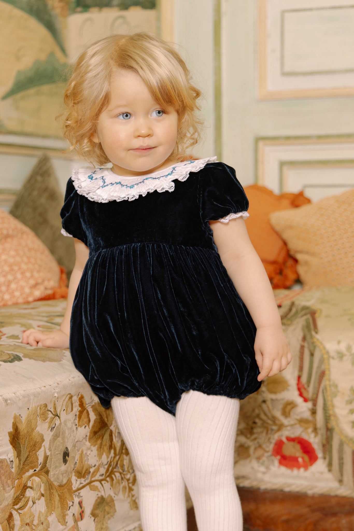 Young child wearing Celestine Navy Velvet Smocked Romper in a decorated room.