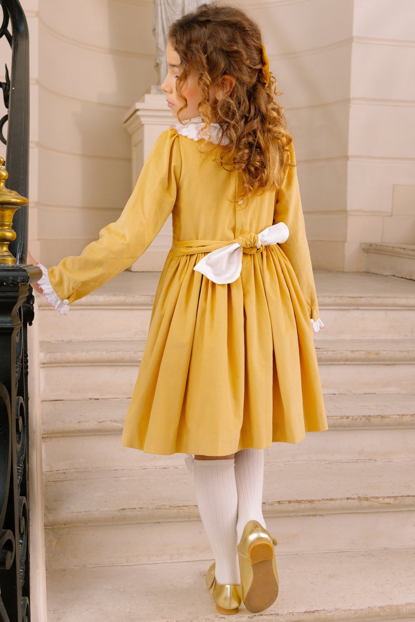 Young girl in Chiara Yellow Smocked Dress standing on a staircase