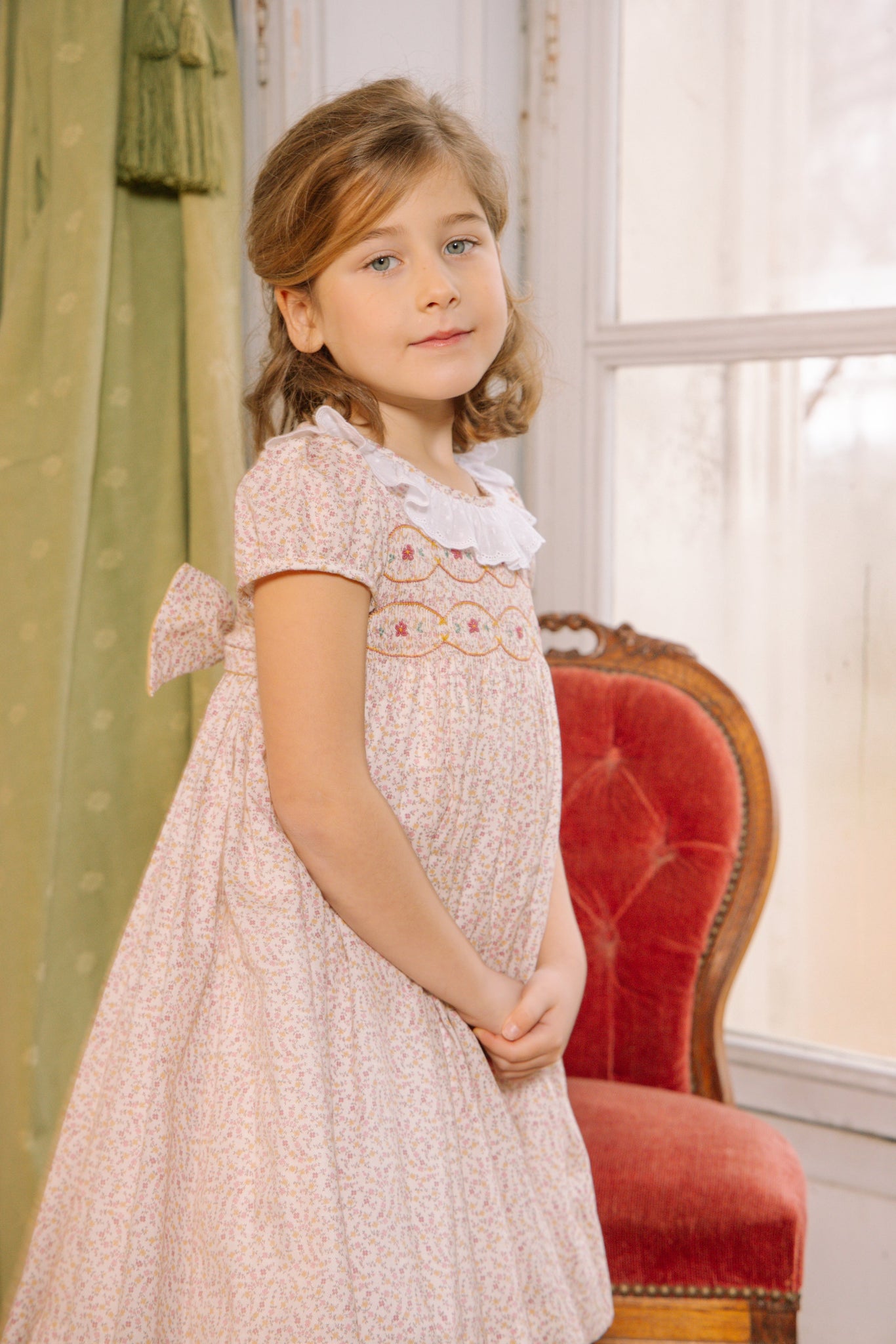 Young girl in Isadora Short Sleeve Floral Smocked Dress standing indoors