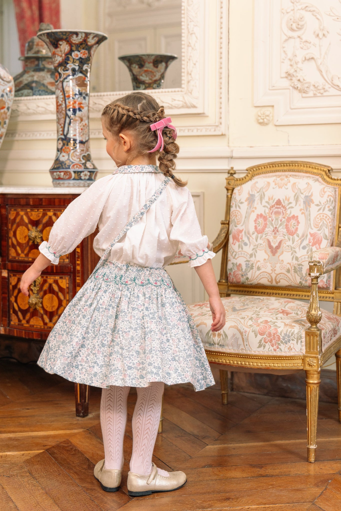 Young girl in Marie Blue Floral Smocked Skirt Blouse Set standing in a room with furniture and decor.