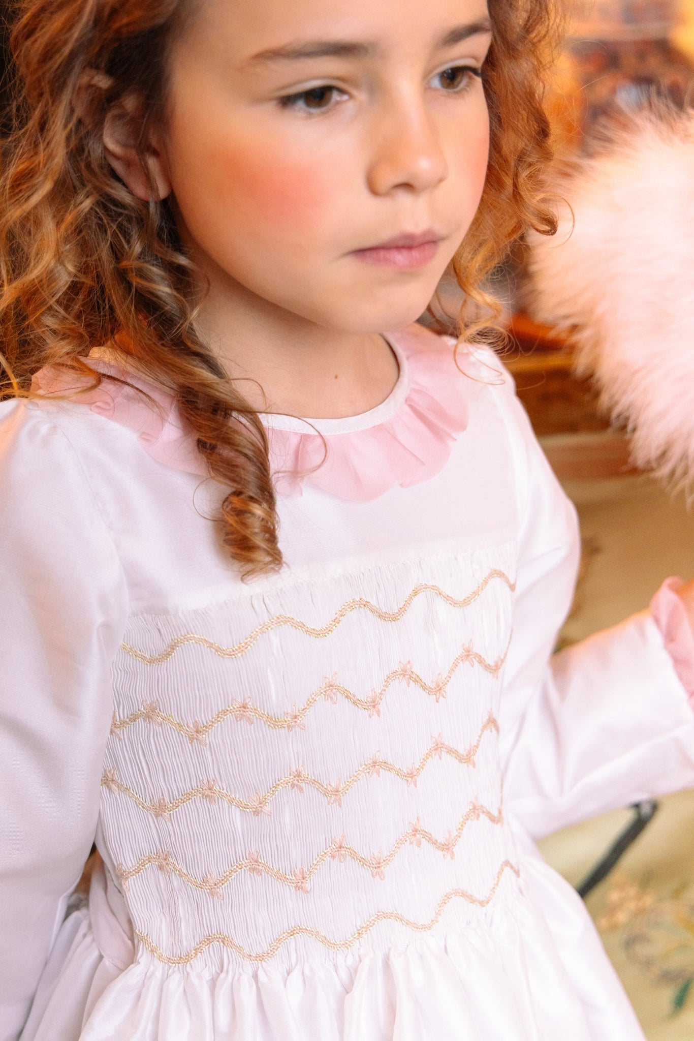 Young girl wearing Sofia White Taffeta Long Sleeve Smocked Dress indoors