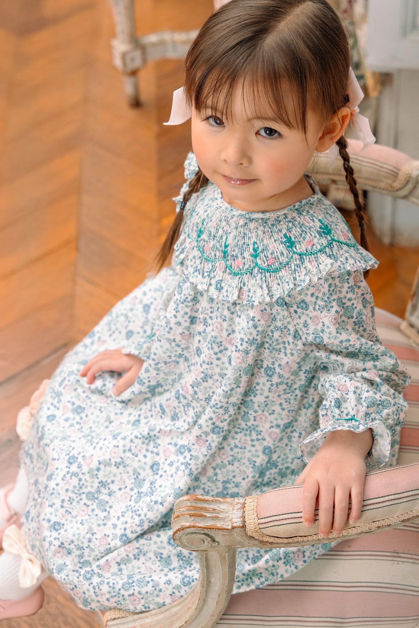 A young child sitting on a bench, wearing Yse Blue Floral Long Sleeve Bishop Dress